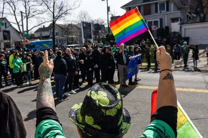 A man dressed in green holds a rainbow flag and cheers for the marchers.